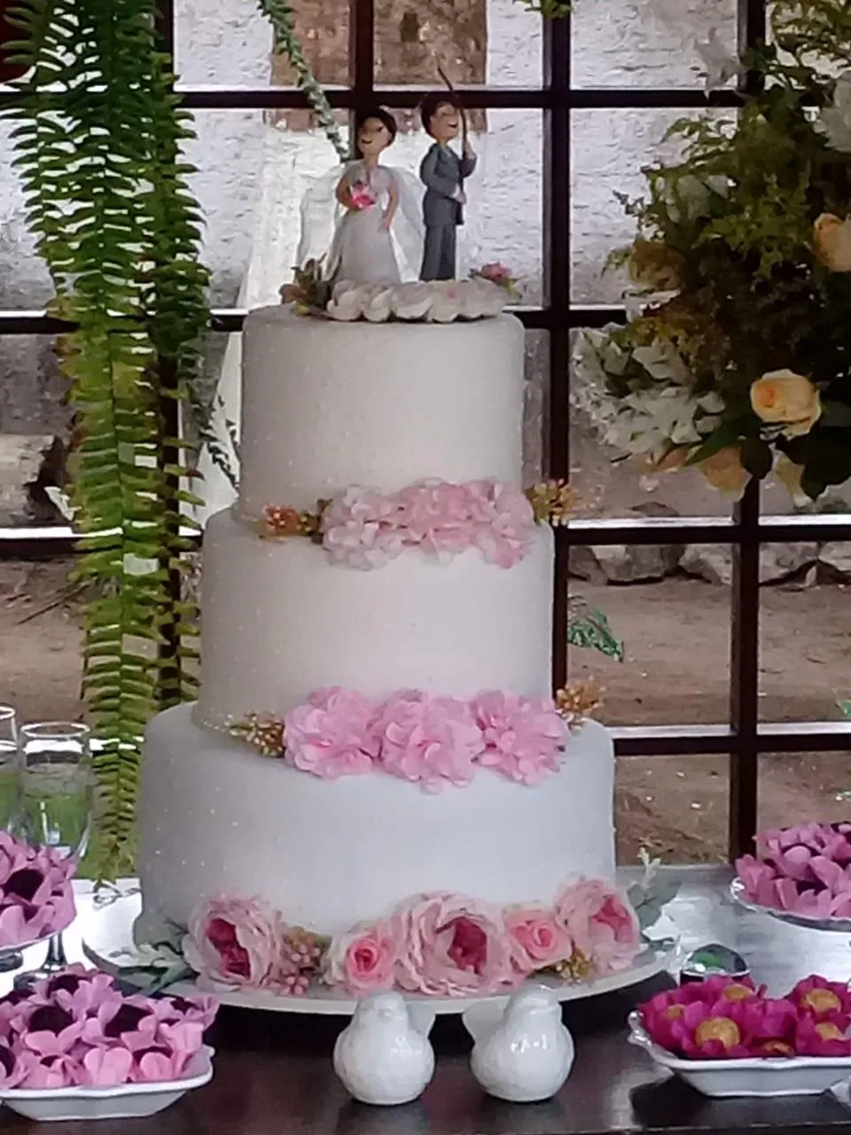Bolo de casamento de três andares entre samambaias e flores
